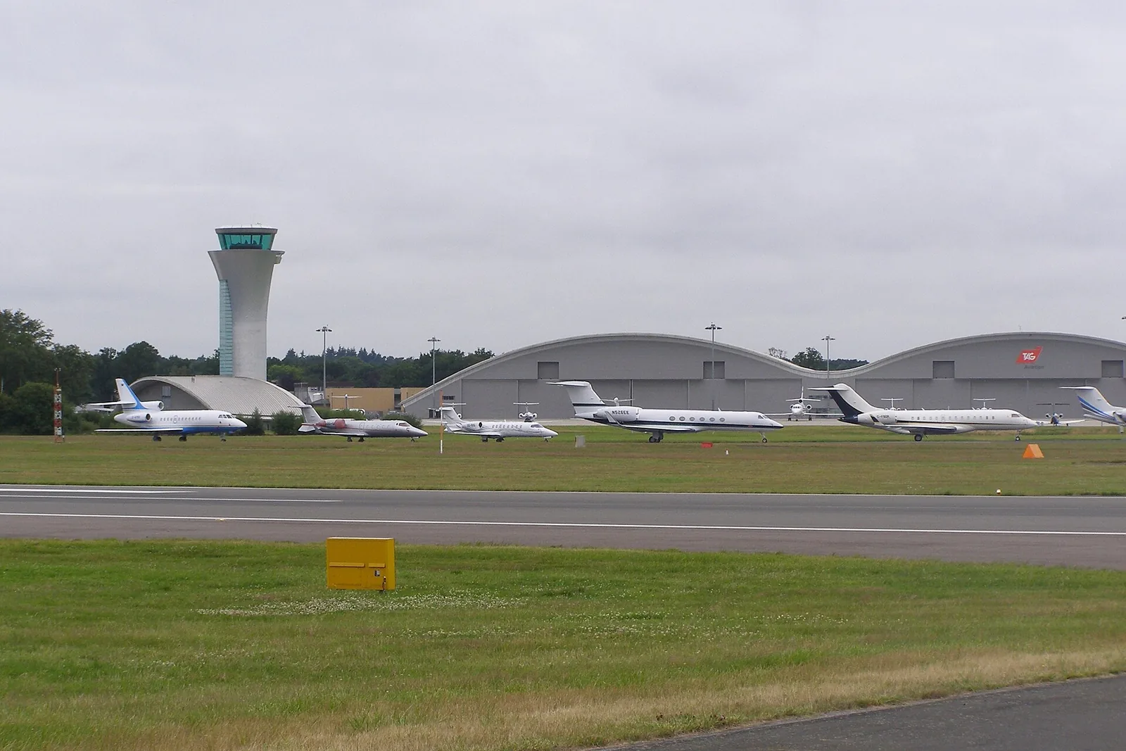 Business jets parked at Farnborough Airfield, with its control tower and curved hangars behind